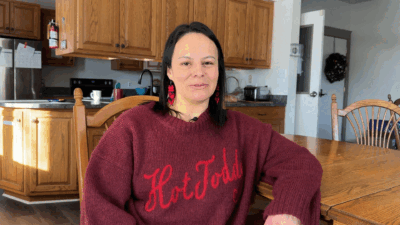 A woman wearing a red sweater sits in a kitchen.