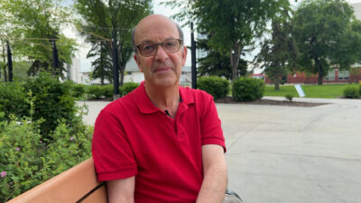 A man with glasses and a red shirt smiles into the camera.